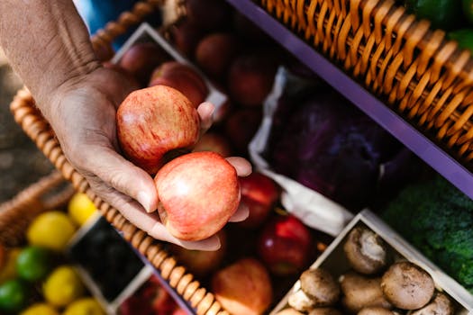 A hand holding fresh apples at a vibrant outdoor farmers market.