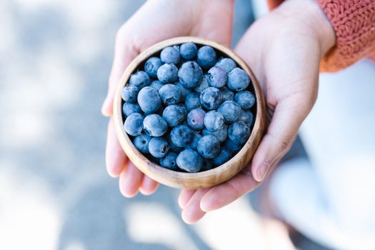 A close-up of fresh blueberries held in a wooden bowl by hands, perfect for healthy eating themes.