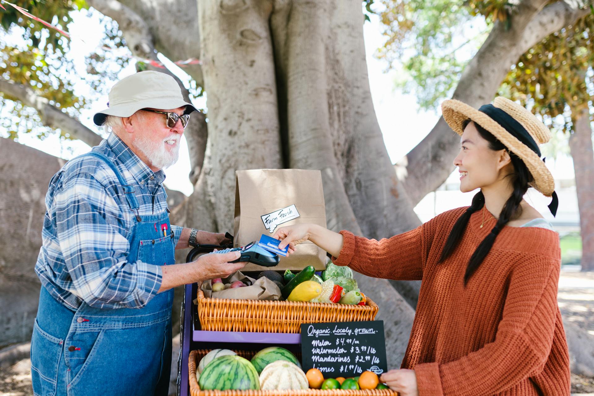 A Woman Paying Using Her Credit Card while Talking to the Vendor Holding a Payment Terminal