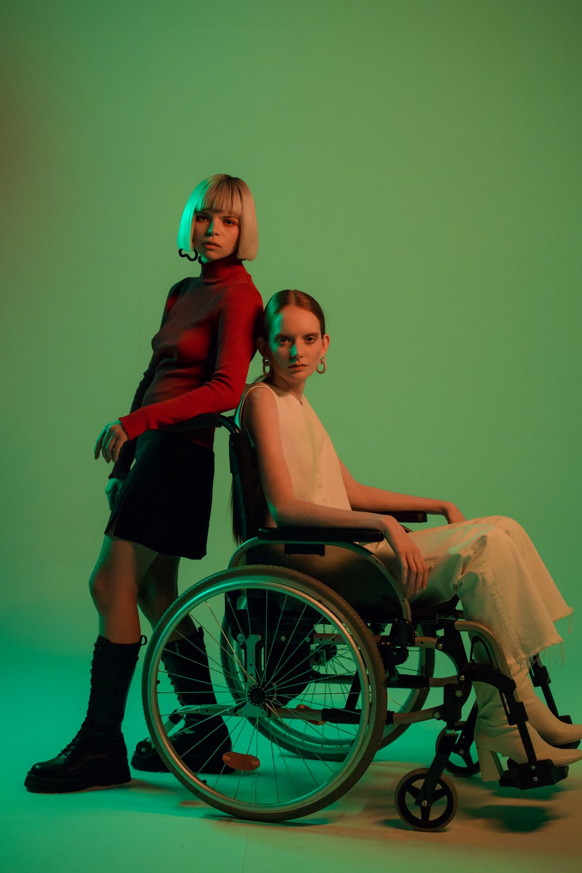 Two fashion models styled together, including a woman using a wheelchair, in a clean studio setting