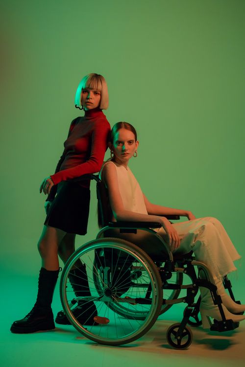 Free Two women in a stylish studio setting, one in a wheelchair, against a light green background. Stock Photo