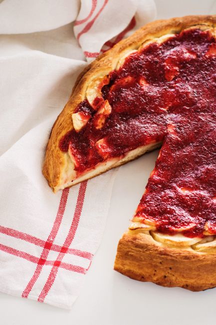 Mouthwatering berry tart with a slice missing on a white surface with a rustic napkin.