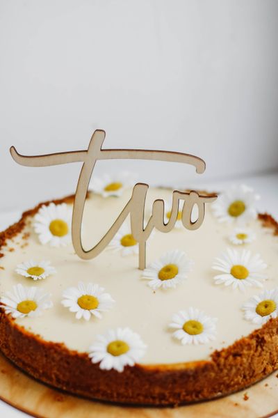 Cream cake with a cut-wood script topper and daisies, photo by Kristina Paukshtite on Pexels