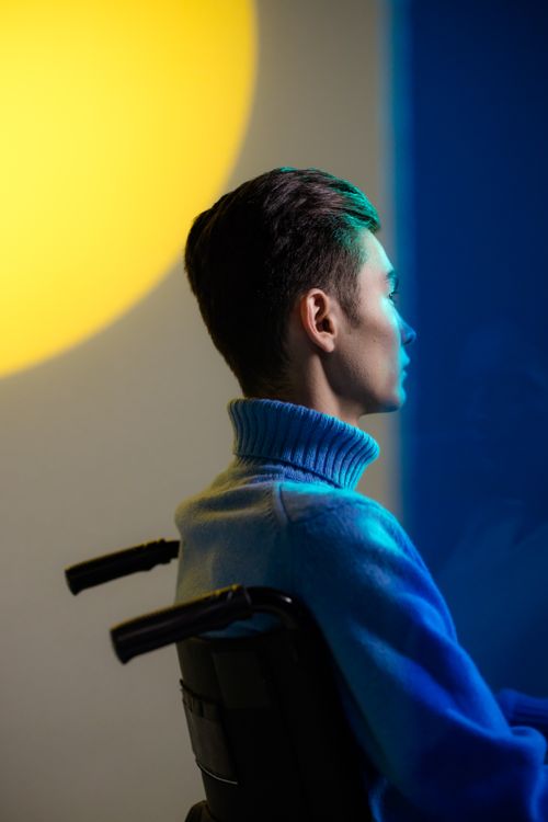 Free Side view of a young man in a wheelchair, highlighted by dramatic light and shadow. Stock Photo