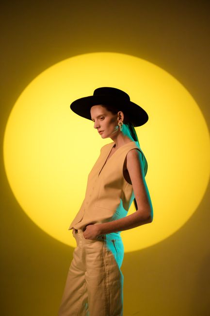 Fashionable woman in a boater hat under colored lighting in a studio setting.