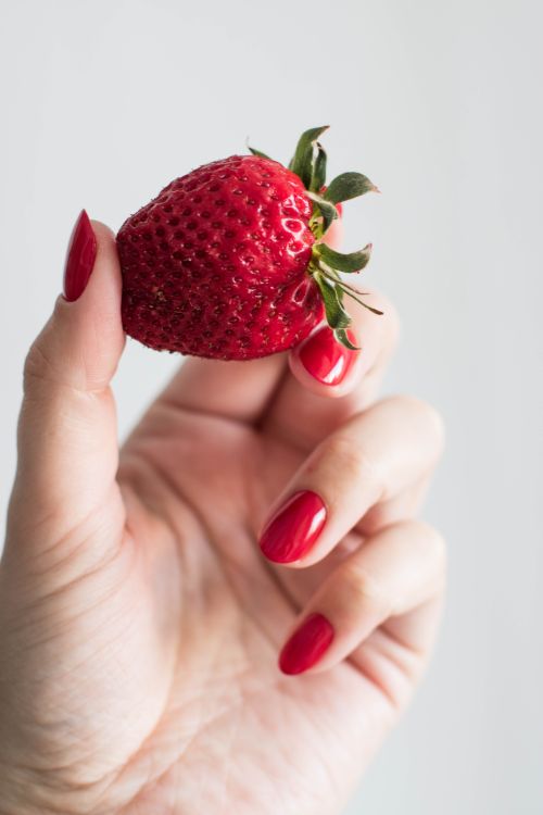 Free A hand with polished nails holding a vibrant red strawberry, showcasing freshness. Stock Photo