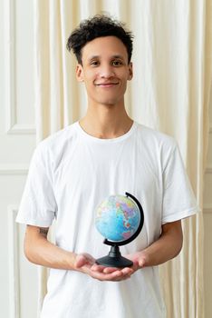 Smiling young man in a white shirt holds a globe, symbolizing global awareness. 8542364