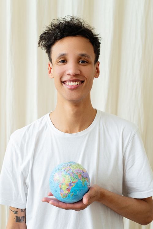 Free Portrait of a smiling young man holding a small globe, symbolizing global unity. Stock Photo