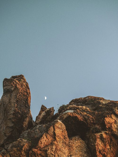 Free Low-angle view of rugged rock formations against a clear sky with the moon visible. Stock Photo