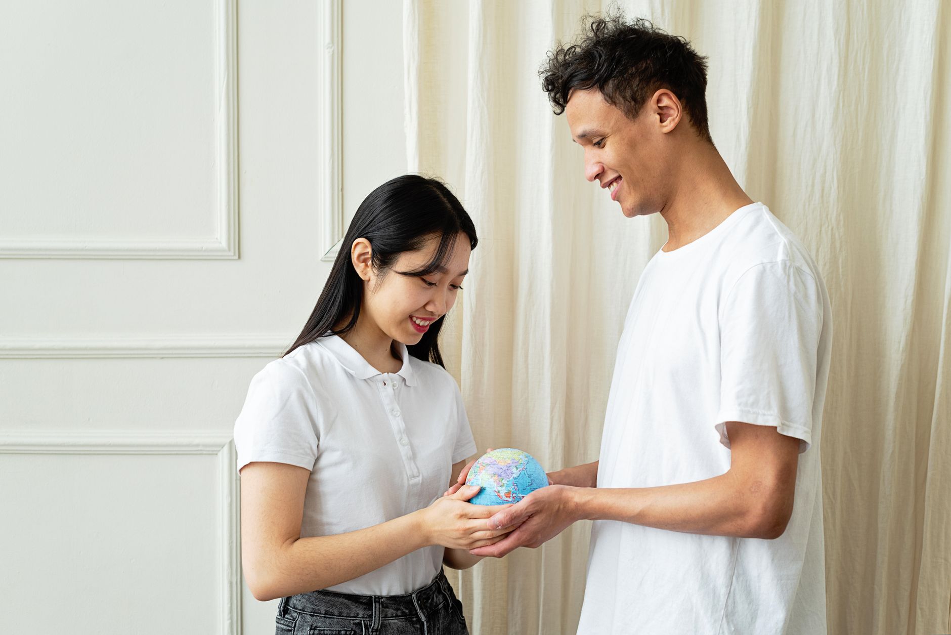 A diverse couple in white shirts holds a small globe, symbolizing unity and ecology indoors.