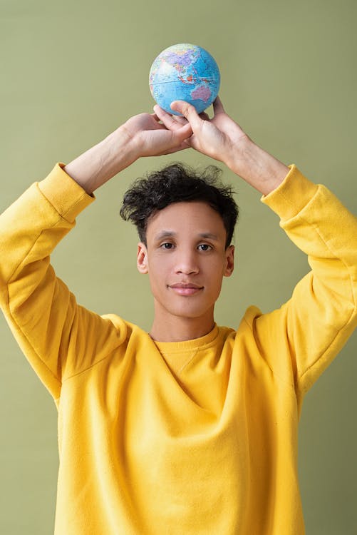 Man in Yellow Sweater holding a Globe 