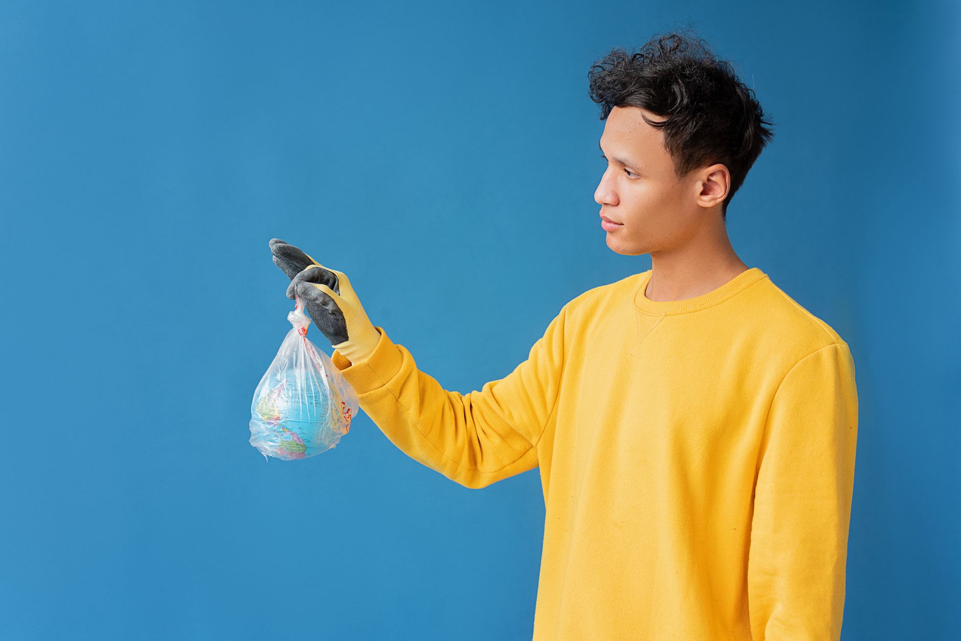 A person in a yellow sweater holds a globe in a plastic bag, highlighting environmental concerns.
