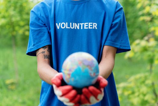 Close-up of a volunteer in blue shirt and gloves holding a globe, symbolizing earth protection.