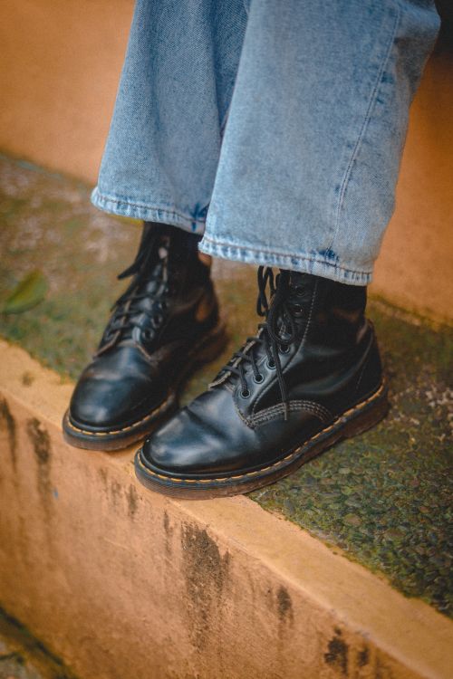 Free Stylish black leather boots paired with denim jeans, captured outdoors on rugged steps. Stock Photo