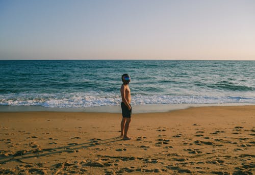 A Shirtless Man Standing on the Beach Sand while Wearing a Helmet