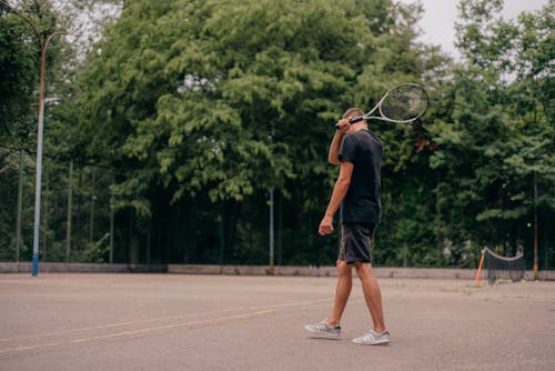 Man in Black Tank holding a Tennis Racket 