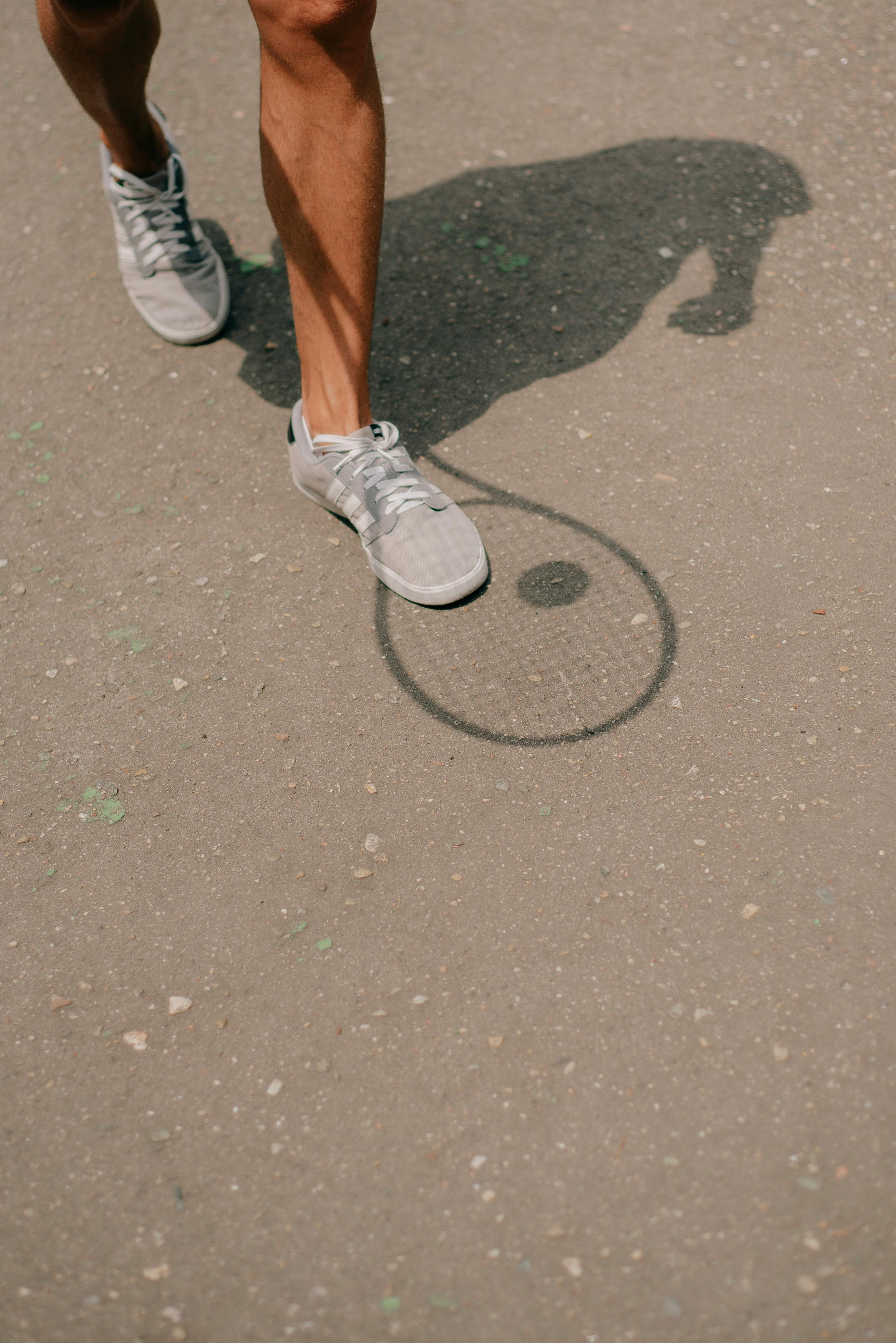 Shadow of a tennis racket and sneakers on asphalt surface, captured in a unique perspective.