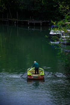 A senior man paddles a boat on a tranquil lake surrounded by lush greenery.