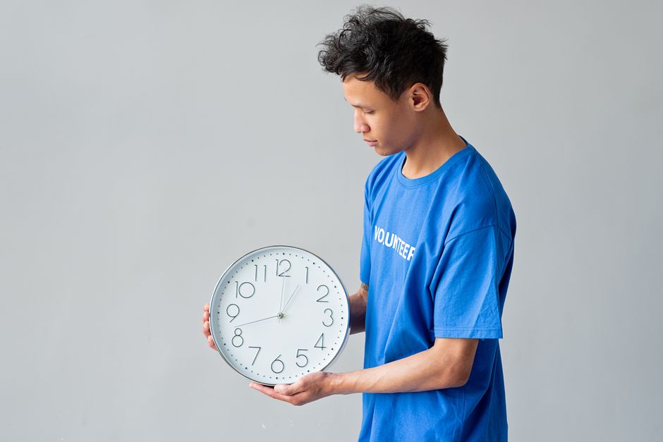 Male volunteer in a blue shirt holds a wall clock, showing the concept of time management.