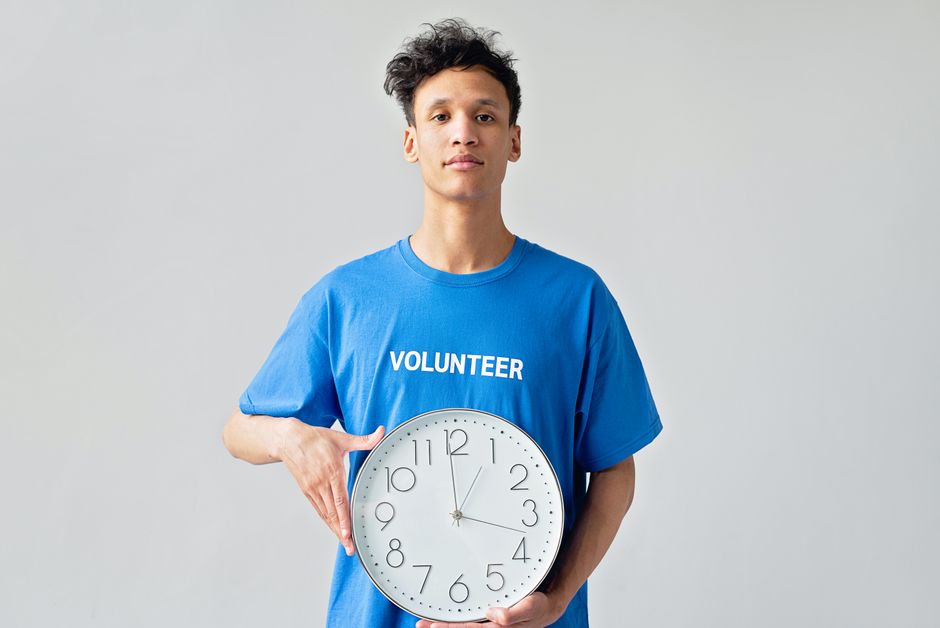 Young male volunteer in blue shirt holding a clock, symbolizing time management.