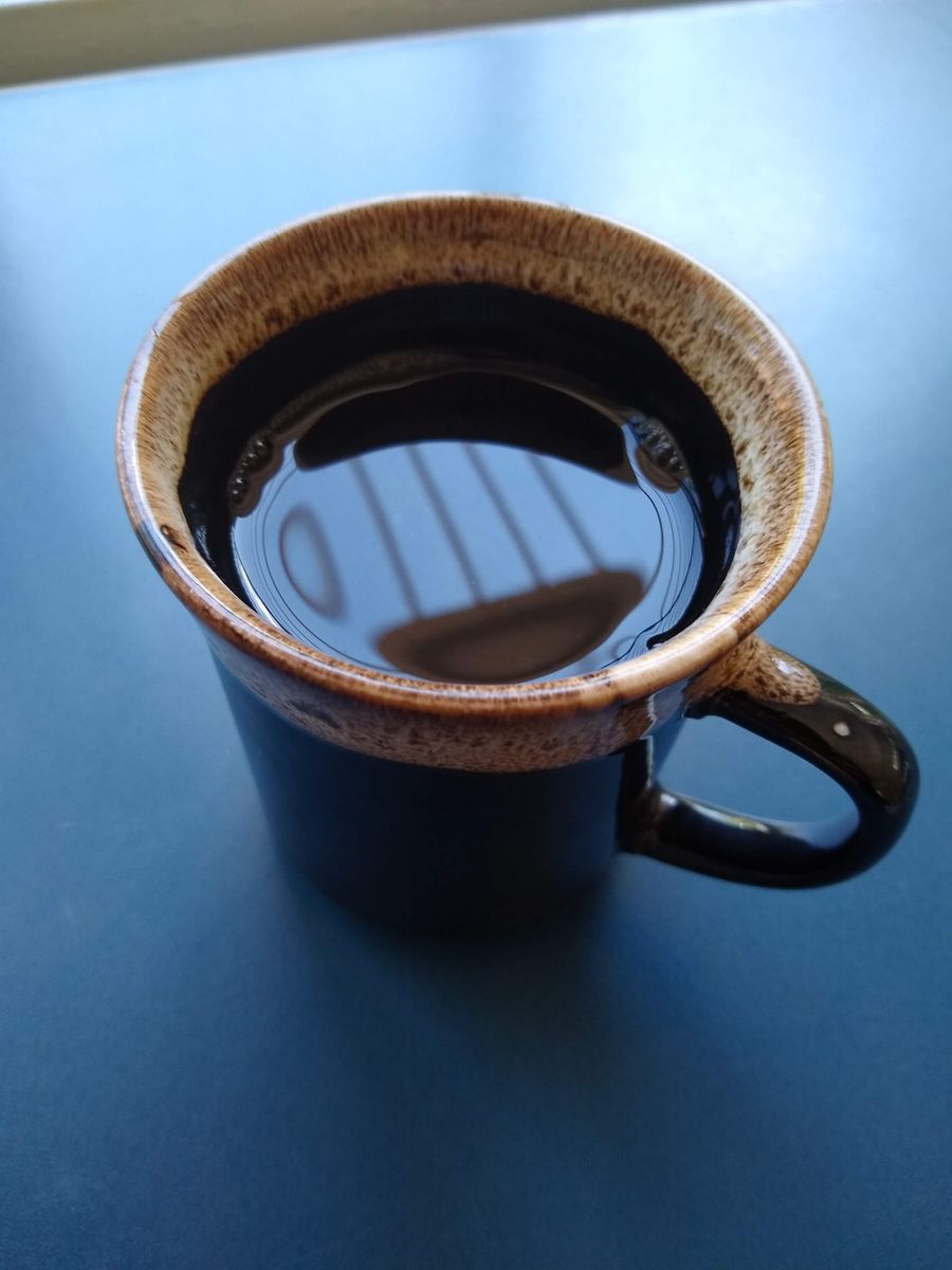 A dark ceramic cup of black coffee on a blue surface, morning light