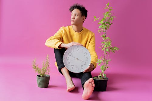 Free Photo of a Man Holding A Wall Clock Beside Green Plants With Purple Background Stock Photo