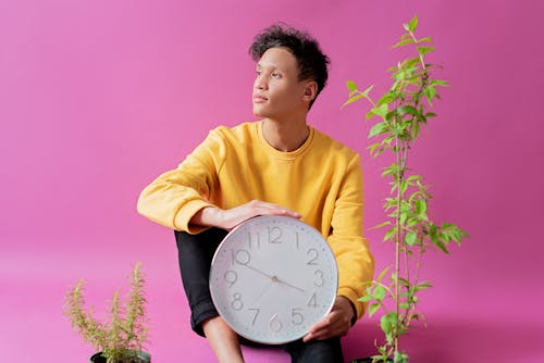 Man in Yellow Sweater holding a Clock 