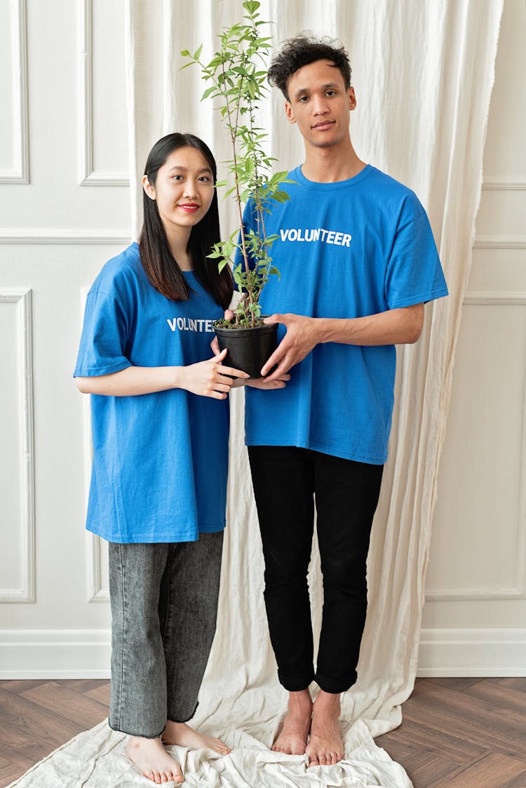 A Man And Woman In Blue Shirt Standing While Holding A Potted Plant