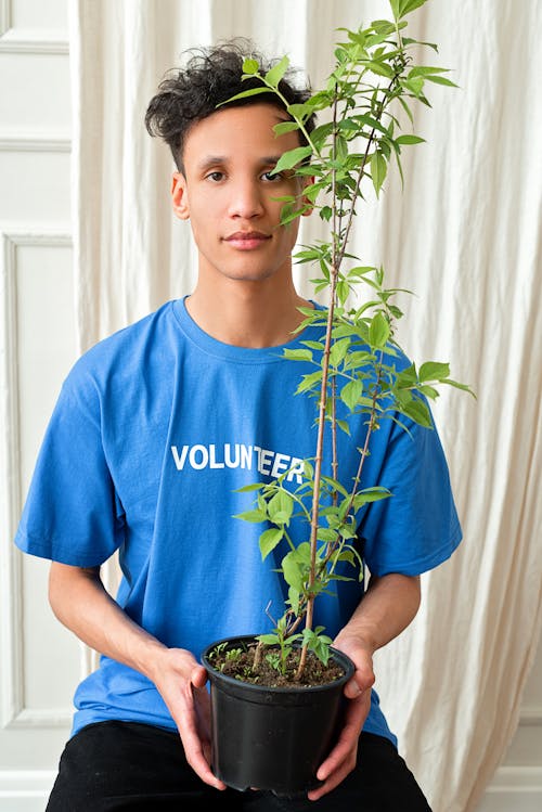A Man in Blue Shirt Holding a Potted Plant with Green Leaves