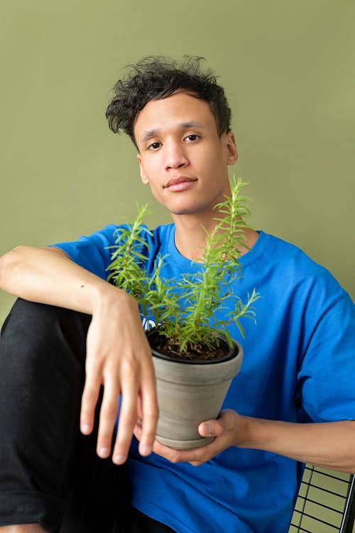 A Man in Blue Shirt and Pants Holding a Potted Green Plant