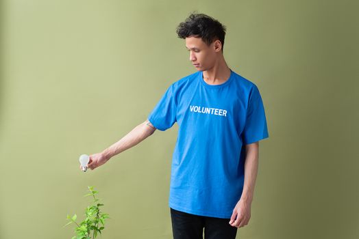 Young volunteer in a blue shirt promoting eco-friendly practices by holding a light bulb next to a plant.