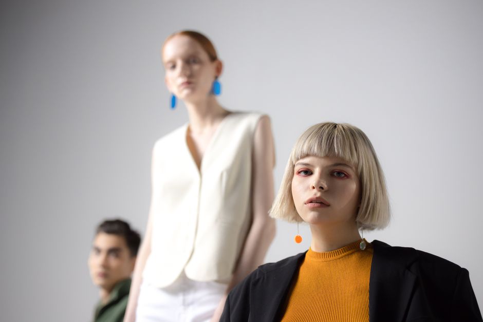 Three stylish models pose in a modern studio fashion shoot on a white background.