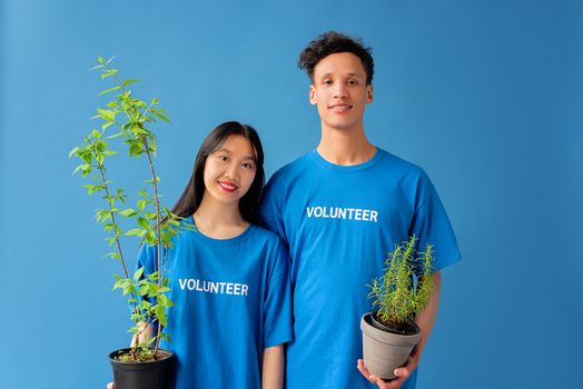 Smiling volunteers holding potted plants against a blue background, promoting environmental awareness.