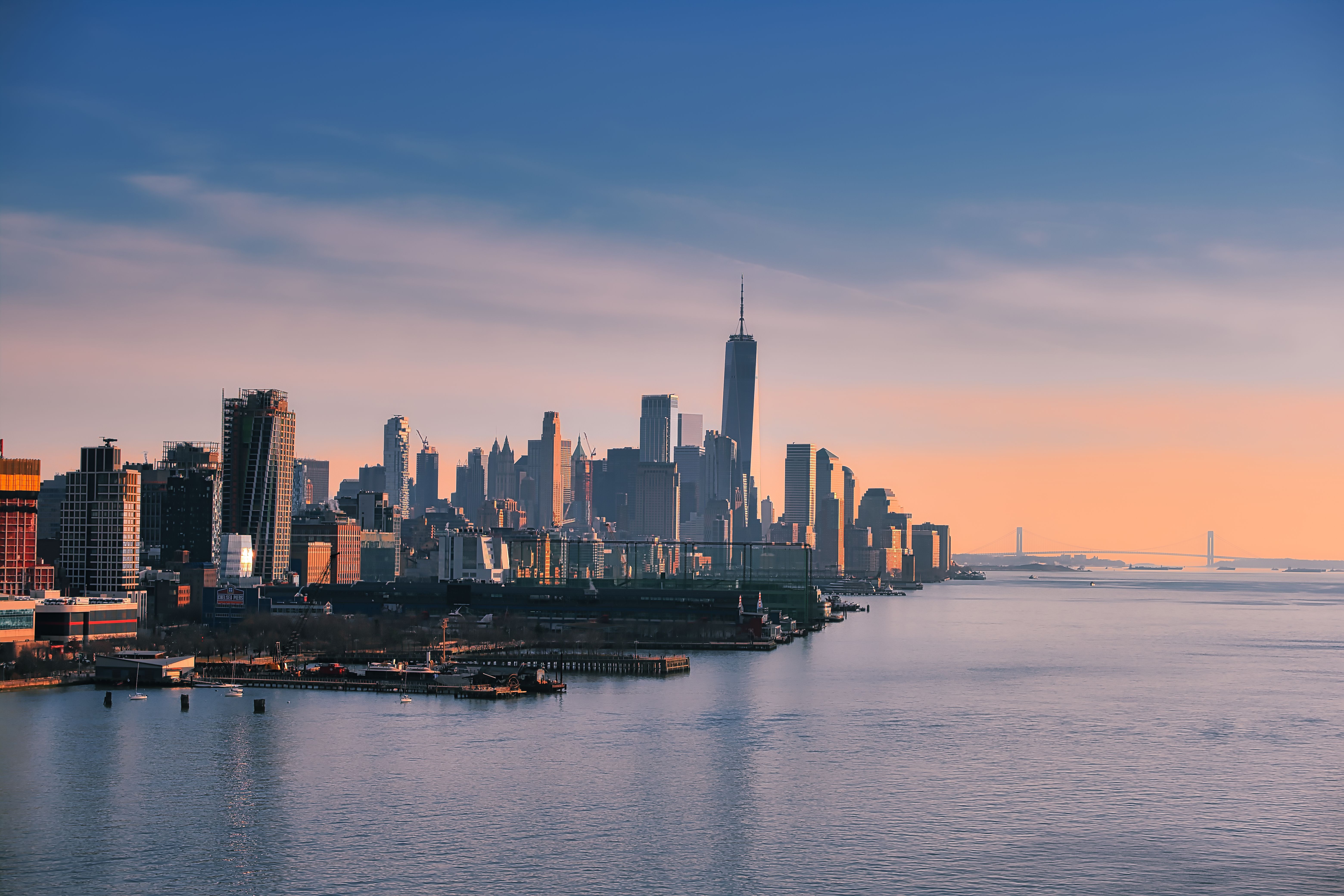 Stunning aerial view of New York City skyline at sunset with calm waters in the foreground.