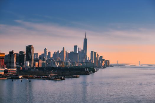 Stunning aerial view of New York City skyline at sunset with calm waters in the foreground.