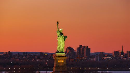 Free Aerial view of the Statue of Liberty at sunset with New York City skyline in the background. Stock Photo