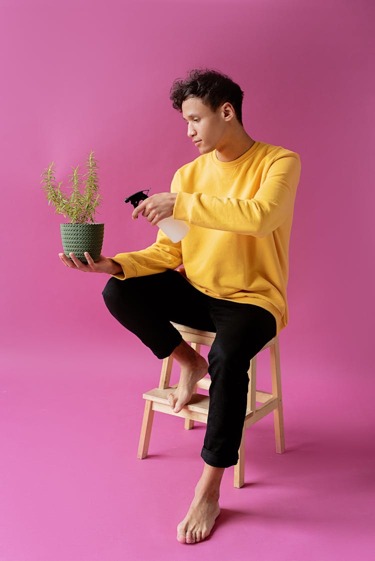 A Man Sitting On A Wooden Chair While Holding A Potted Plant