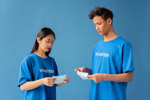 Free Two volunteers in blue shirts handing out face masks for community health support. Stock Photo