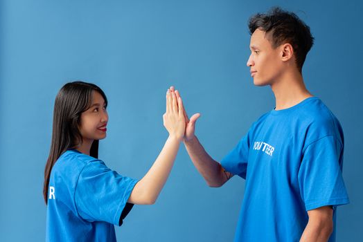 Two young volunteers in blue shirts high-five against a blue background, symbolizing teamwork.