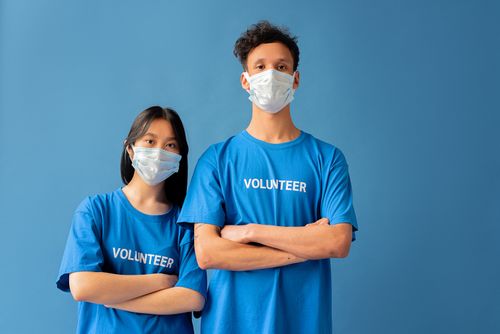 Free Two masked volunteers standing with arms crossed against a blue backdrop. Stock Photo