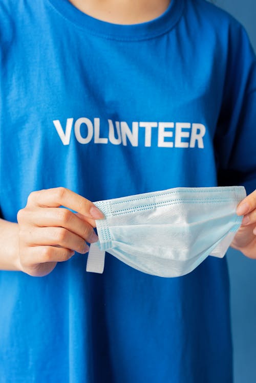 Free A Person Wearing a Blue Volunteer Shirt Holding a Face Mask Stock Photo