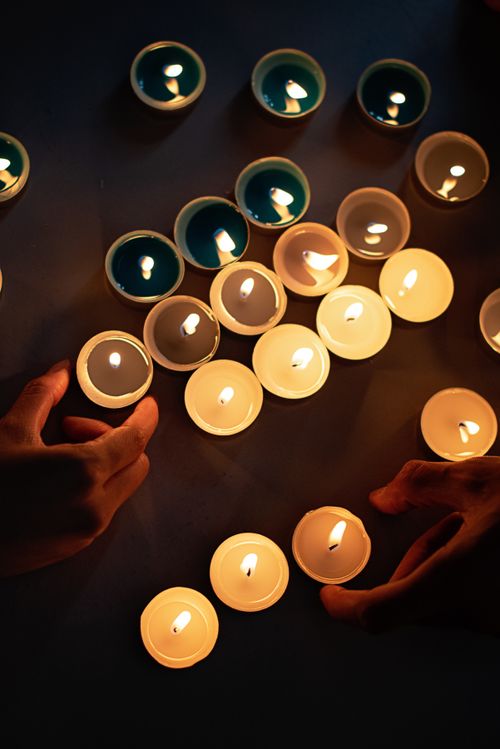 Free A warm, artistic arrangement of tealight candles with visible hands, creating a cozy atmosphere. Stock Photo