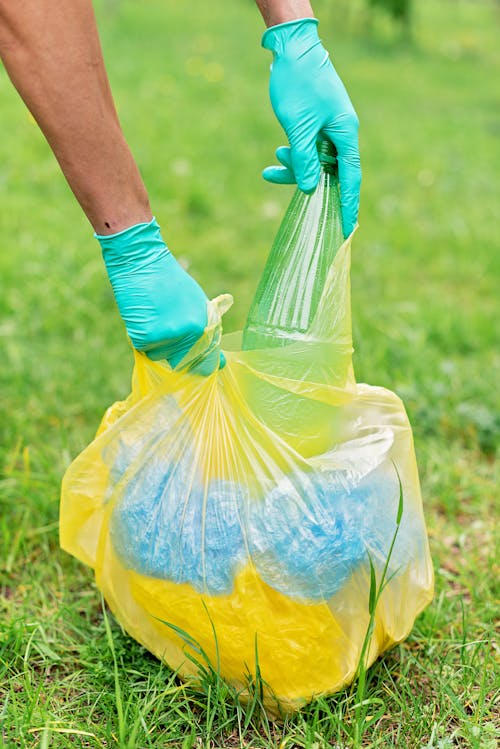 Person in Gloves Holding Yellow Plastic Bag With Recyclable Materials