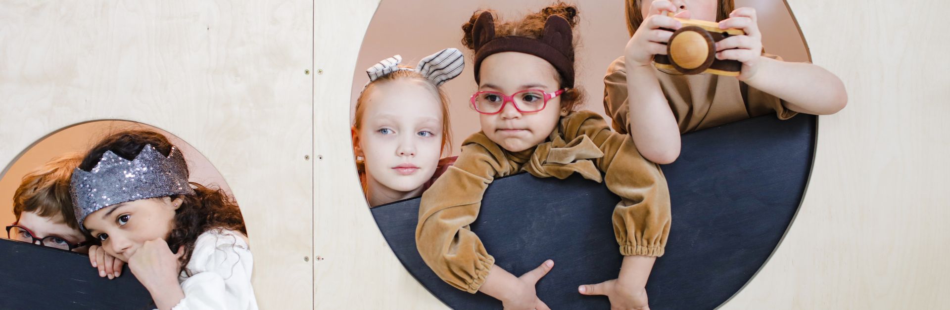 Group of children playing indoors, peeking through circular holes, showcasing imagination and divers
