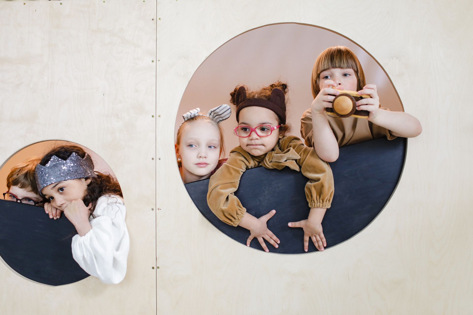 Group of children playing indoors, peeking through circular holes, showcasing imagination and divers