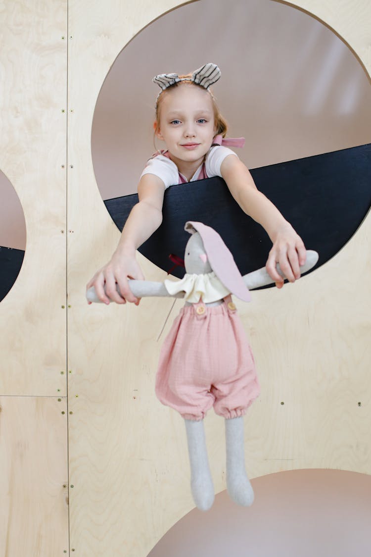 Photo Of A Girl Holding A Doll In A Circle Shaped Window