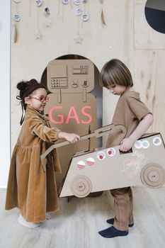 Adorable children role-playing with a cardboard gas station indoors, sparking creativity and imagination.