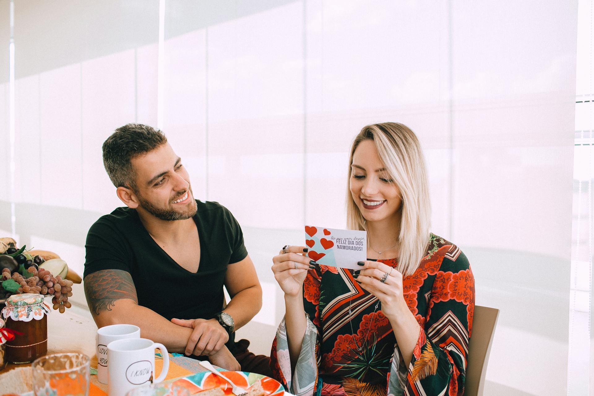 Couple smiling while exchanging a heartfelt Valentine's Day card indoors.