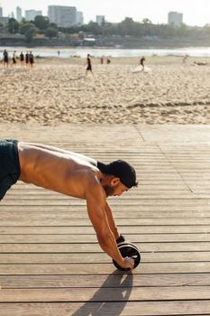 A muscular man works out with an ab roller on a sunny beach boardwalk.