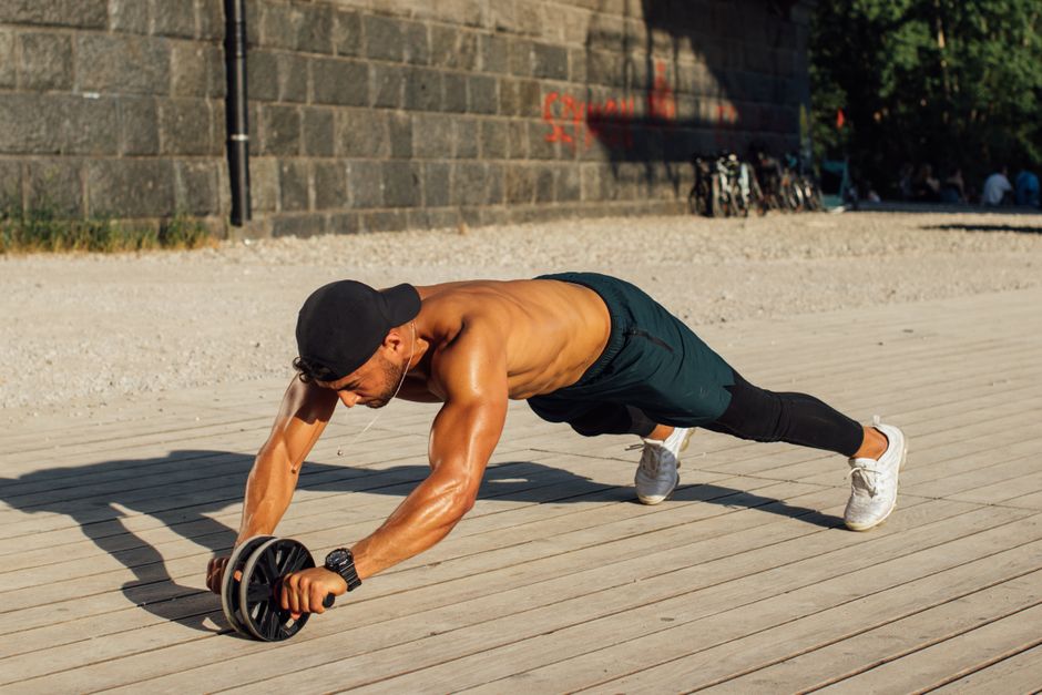Fit man in outdoor workout using ab roller, showcasing strength and fitness.
